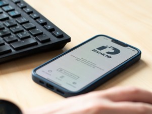 A person holding a smart phone with BankID visible on the screen, next to a keyboard.