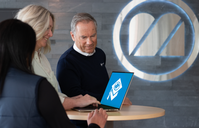 A man and a woman looking at a laptop showing Monitor Academy logo