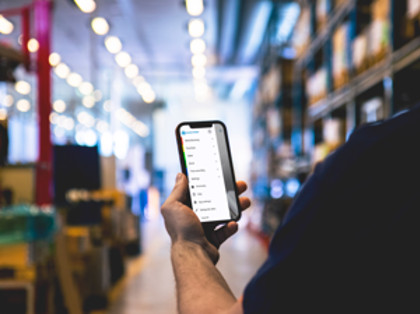 A person in a warehouse holding a cellphone displaying Monitor Mobile menu. 
