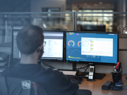 A man sitting in a manufacturing environment, in front of a computer using Monitor ERP system. 