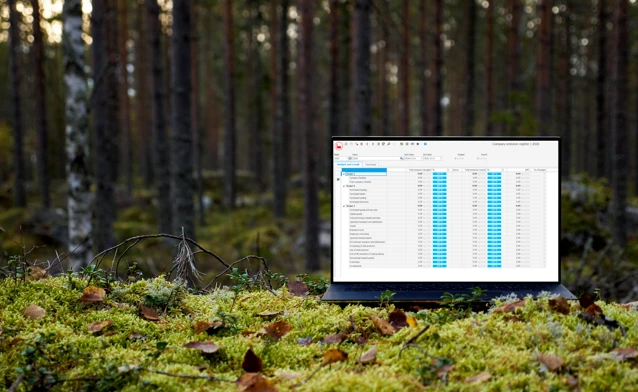 A laptop computer displaying Monitor ERP and its sustainability functionality sitting on top of a moss covered ground surrounded by trees.