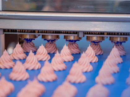 A conveyor belt filled with lots of pink cookies.