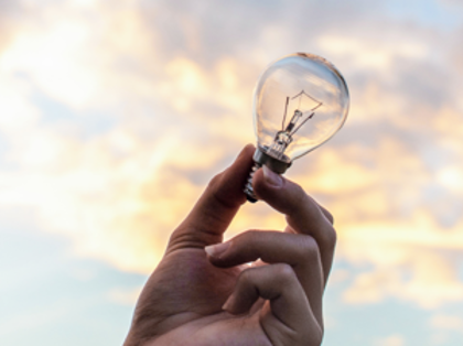 A hand holding a light bulb in front of a cloudy sky.
