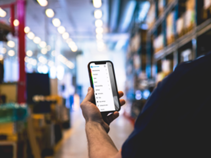 En person i ett lager håller en mobiltelefon som visar menyn för Monitor Mobile.