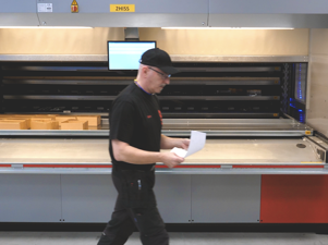 Warehouse employee in a black shirt is walking by a machine.