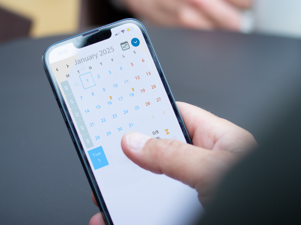 A person holding a cell phone with a calendar on the screen.