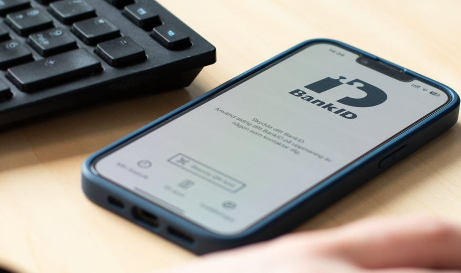 A person holding a smart phone with BankID visible on the screen, next to a keyboard.