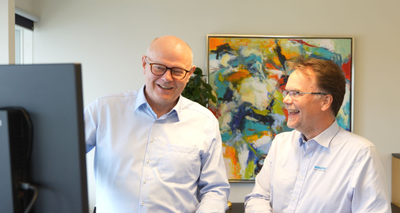 Two men standing in front of a computer monitor.